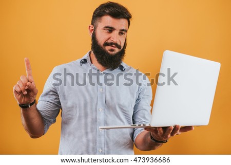portrait of handsome smiling man isolated on yellow studio background posing to the camera and making funny faces, got idea, pointing to the monitor working on laptop computer