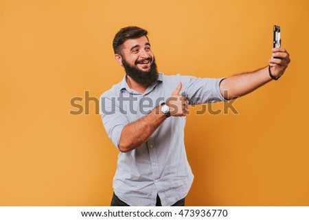 portrait of handsome smiling man isolated on yellow studio background posing to the camera and making funny faces and selfie