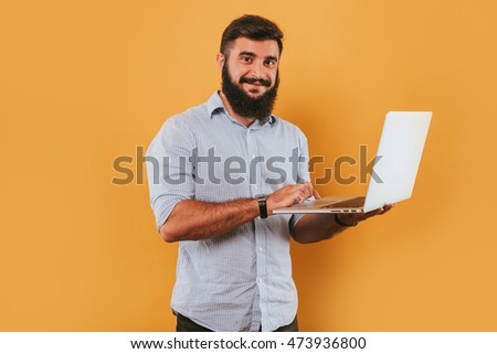 portrait of handsome smiling man isolated on yellow studio background posing to the camera and making funny faces, got idea, pointing to the monitor working on laptop computer