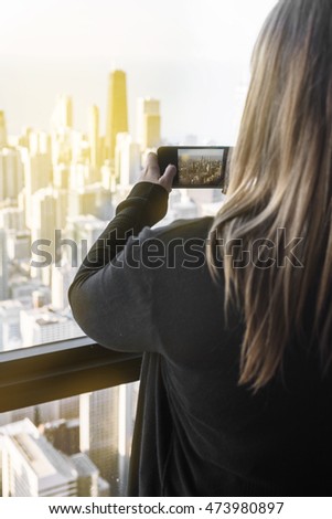 woman taking picture of beautiful city sunset on her phone, seen from a large building. 