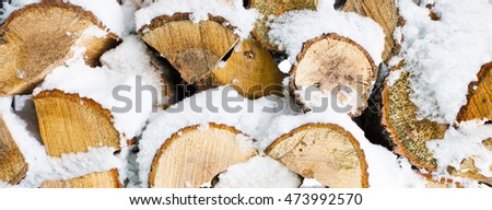Winter background texture pattern with stacked dry chopped firewood logs covered with snow. Firewood pattern