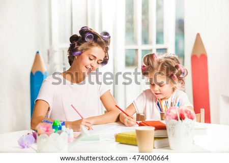 The young mother and her little daughter drawing with pencils at home