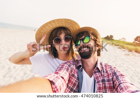 Happy young  couple in love making a selfie on phone at the beach on a sunny summer day. Pretty girl and her handsome boyfriend with beard having fun, crazy emotional faces , laughing.