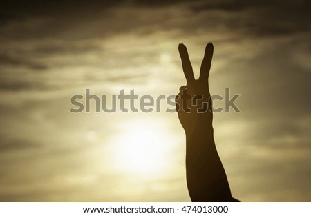 woman hand raising two fingers on sunset background,fighting with everything concept,life is going on concept,winner with fighting