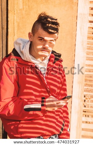 Young man posing outdoor in red jacket covered with beautiful shadow at sunny day autumn fall season