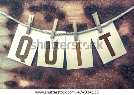 The word "QUIT" stamped on cards and pinned to an old piece of twine over a rusted metal background.