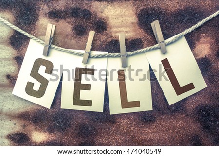The word "SELL" stamped on cards and pinned to an old piece of twine over a rusted metal background.