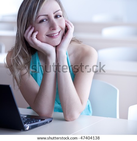 pretty young college student in class, using a laptop computer, smiling