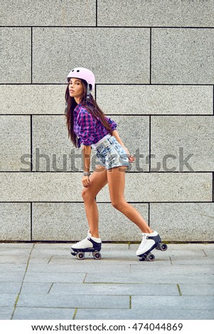 Beautiful young girl skating on roller skates on the background of gray wall in a park. Full length of happy young woman roller skating.