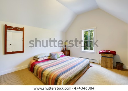 Simple design of attic bedroom with vaulted ceiling. Wicker box, colorful striped bedding and wooden framed mirror. Northwest, USA