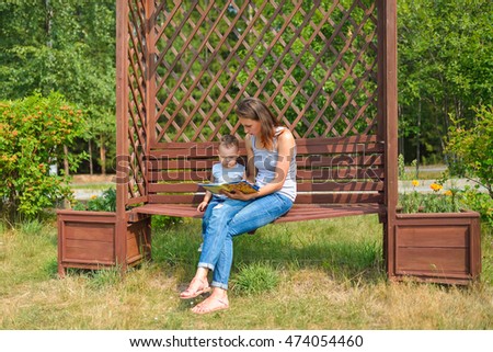 Mother with son sitting on a bench in  park and reading  book