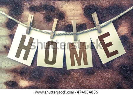The word "HOME" stamped on cards and pinned to an old piece of twine over a rusted metal background.