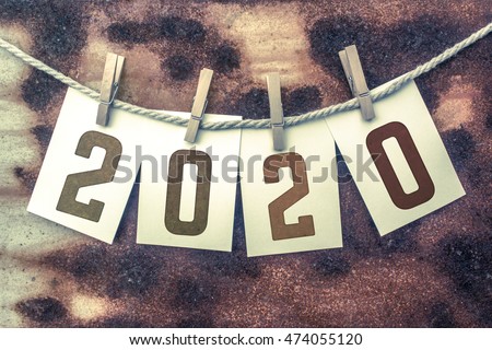 The word "2020" stamped on cards and pinned to an old piece of twine over a rusted metal background.