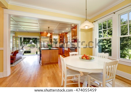 Open plan dining room interior. Yellow walls and hardwood floor. Kitchen and living room in the background. Open doors to the back yard. Northwest, USA