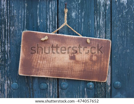 Mock up wooden textured sign with rounded corners and brown paint traces hanging on natural linen rope on a rusted metal nail on blue scratched planking door background