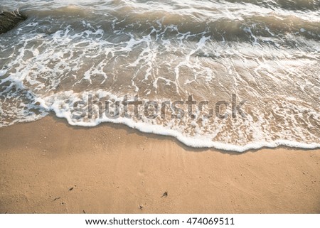 Soft wave of the sea on the sand beach with sunlight. Tropical sandy beach background with copy space. Top down view.