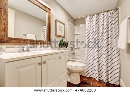 White tones Bathroom with vanity cabinet and wooden framed mirror. Decorated with picture, plant pot and striped curtain. Northwest, USA