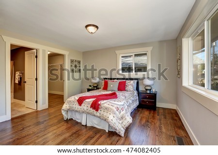 View of tidy bedroom with hardwood floor and colorful bed with red pillows. Has doors to the bathroom and empty closet. Northwest, USA