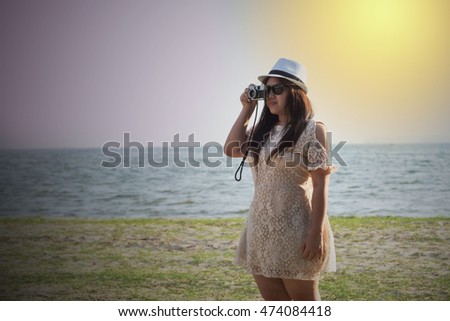 woman take photo with film camera by sea beach ocean on twilight time sunset on beach in white dress and white hat