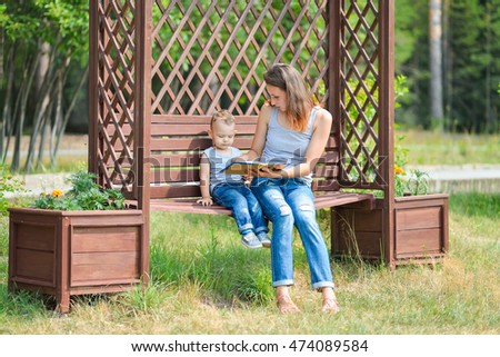 Mother with son sitting on a bench in park and reading book