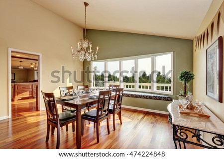 Elegant dining room with contrast olive wall, vaulted ceiling, comfortable window seat and hardwood floor. Chandelier in vintage style and table setting set. Northwest, USA