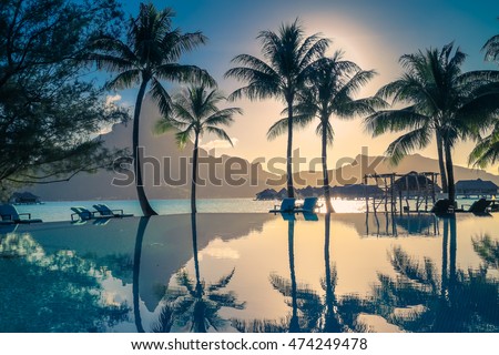 Sunset in Bora Bora , French Polynesia . Palm trees and Mount Otemanu reflected in the pool. Retro style color tones. Royalty-Free Stock Photo #474249478