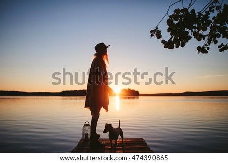 girl in a poncho and a hat with lamp standing back to the view of the sunset on the lake