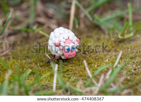 Plasticine world - little homemade white sheep with blue eyes on a green background, selective focus and place for text