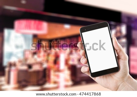 right hand using smartphone with blank screen on Abstract blur people shopping in cosmetic store or beauty store in department store, urban lifestyle concept.