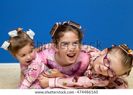 Three silly sisters, a little hyper before bedtime, hug in a pile on the floor while wearing curlers in their hair.  They are ready for bed in their pajamas.