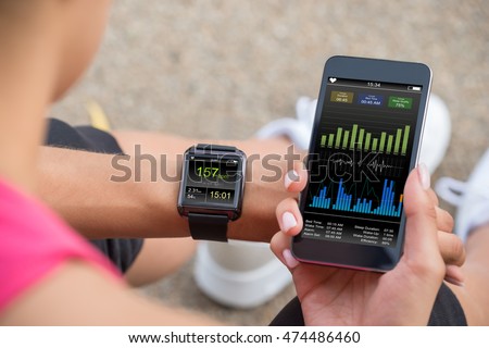 Female Runner Looking At Her Mobile And Smart Watch Heart Rate Monitor Royalty-Free Stock Photo #474486460