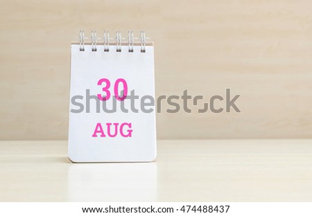 Closeup surface note book with pink 30 aug word  in page on blurred brown wood desk and wood wall textured background with copy space under window light