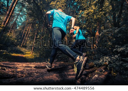 Two athlete running through the forest crossing wood barrier Royalty-Free Stock Photo #474489556