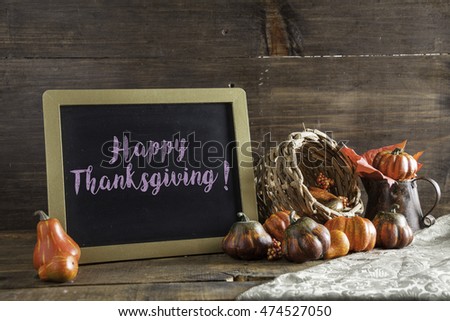 Happy Thanksgiving Written In Purple Chalk On Black Chalkboard Background On Aged Wood Table With Thanksgiving Decorations In Selective Focus.