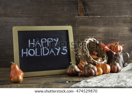 Happy Holidays Written In Blue Chalk On Black Chalkboard Background On Aged Wood Table With Thanksgiving Decorations In Selective Focus.