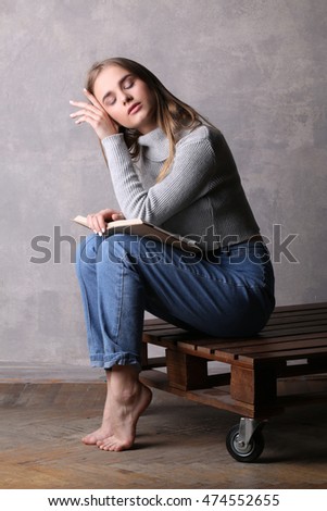 Sitting girl with book touching her face. Gray background