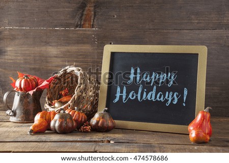 Happy Holidays Written In Blue Chalk On Black Chalkboard Background On Aged Wood Table With Thanksgiving Decorations In Selective Focus.
