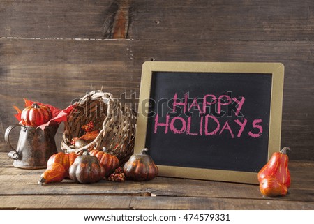 Happy Holidays Written In Red Chalk On Black Chalkboard Background On Aged Wood Table With Thanksgiving Decorations In Selective Focus.