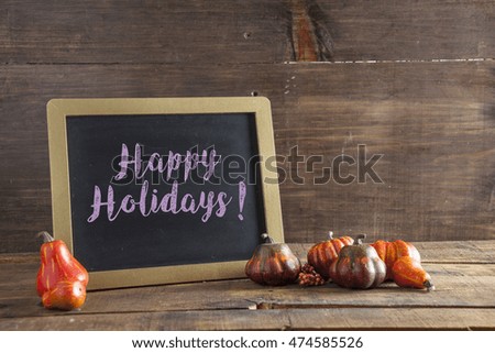 Happy Holidays Written In Purple Chalk On Black Chalkboard Background On Aged Wood Table With Thanksgiving Decorations In Selective Focus.