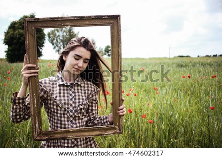 Beautiful hipster woman in retro stylish dress posing with picture frame in poppies field