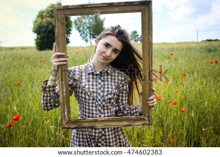 Beautiful hipster woman in retro stylish dress posing with picture frame in poppies field