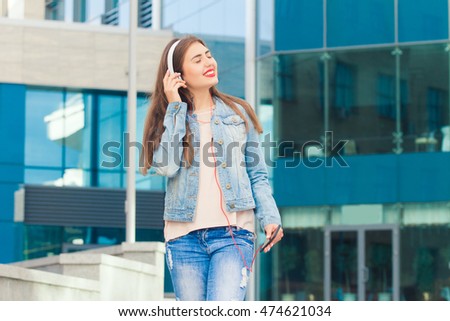 Beautiful girl listening music in headphones and standing on a colorful blue background . She has a beautiful smile .The concept of good music and fun