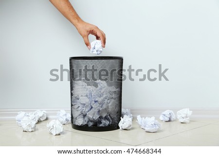 Male hand throwing crumpled paper into metal trashcan Royalty-Free Stock Photo #474668344