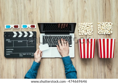 Man holding a ticket and watching a film streaming online with popcorn, 3D glasses and clapboard, movies and cinema concept