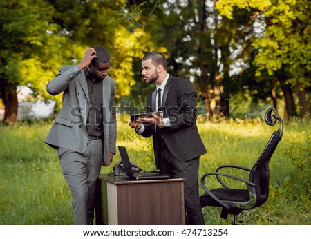 Two young businessman at work in the park. Beautiful background.