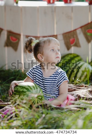 Beautiful little blonde girl of about watermelon stalls. In a striped dress.  with curly tails. Summer. Joy. Watermelons!