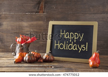 Happy Holidays Written In Yellow Chalk On Black Chalkboard Background On Aged Wood Table With Thanksgiving Decorations In Selective Focus.