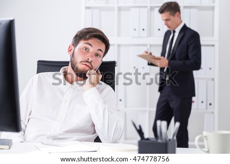 First businessman is talking on phone with business partners. His colleague is making notes in clippad in background. Concept of hard daily work in office