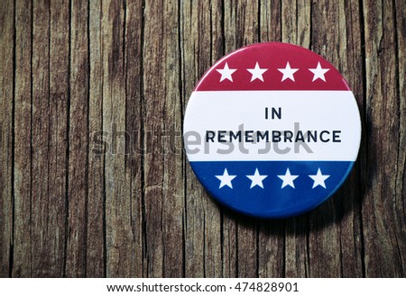 closeup of a pin button with the text in remembrance and the colors and stars of the flag of the United States, on a rustic wooden background