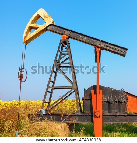 A Small private oil derrick pumps oil on the field. The old handicraft oil rig in the background of the creative industrial design. 